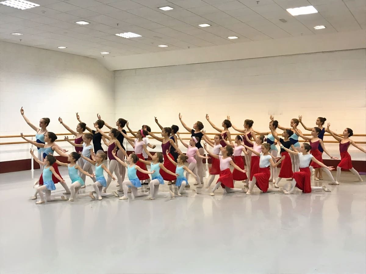 Grupo de bailarines de ballet con coloridos trajes practicando en un luminoso estudio con paredes espejadas.