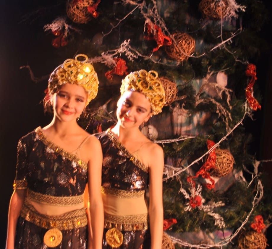 Dos artistas disfrazados de dorado y negro se encuentran de pie frente a un árbol decorado por la noche.