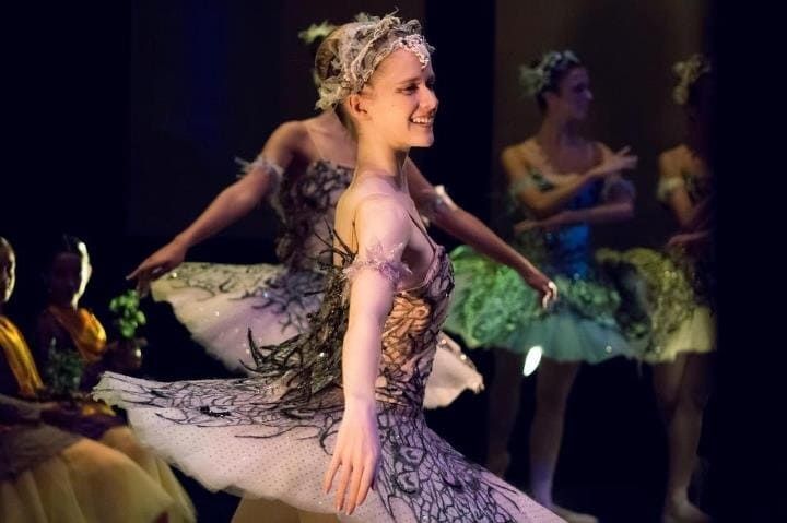 Bailarinas con trajes blancos adornados con encaje dan vueltas sobre un escenario oscuro bajo una iluminación cálida.