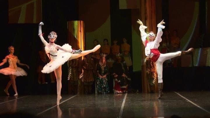 Dos bailarinas de ballet con trajes blancos saltan al escenario durante una actuación.