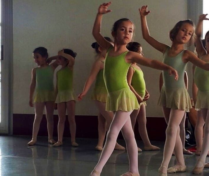 Niñas con leotardos verdes practicando ballet en un estudio, con los brazos levantados en una pose.