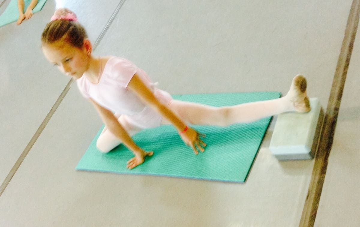 Mujer realizando un estiramiento de yoga sentada sobre una esterilla verde en un estudio.