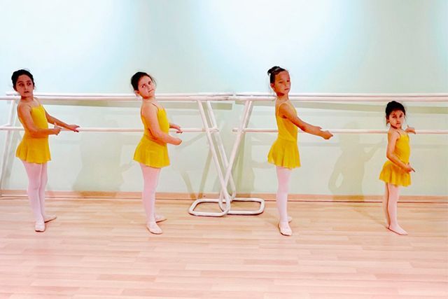 Cuatro bailarinas de ballet con tutús amarillos practicando en una barra en un estudio luminoso.