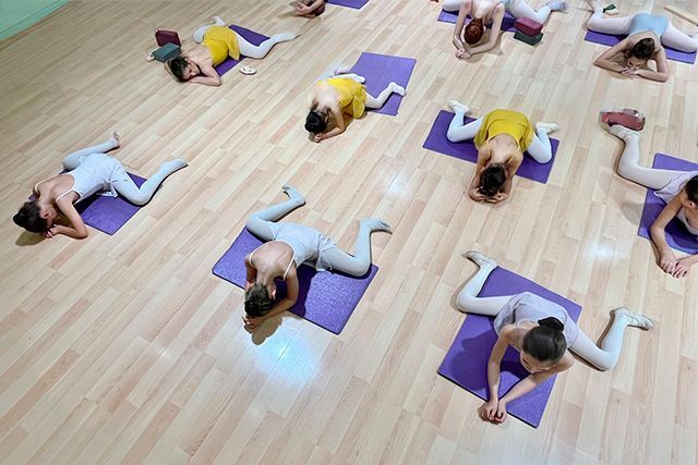 Personas haciendo estiramientos de yoga sobre esterillas en un estudio con suelo de madera.