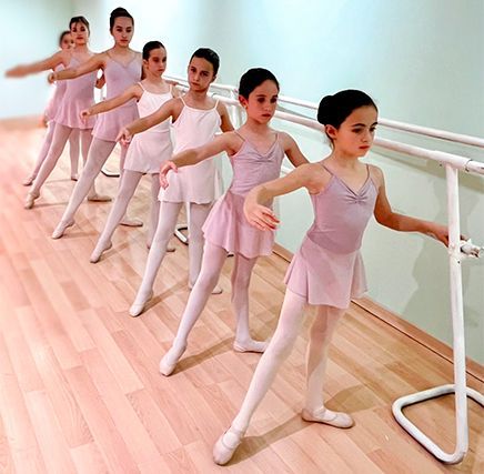 Jóvenes estudiantes de ballet practicando en la barra de un estudio de danza, vestidas con leotardos y medias rosas.