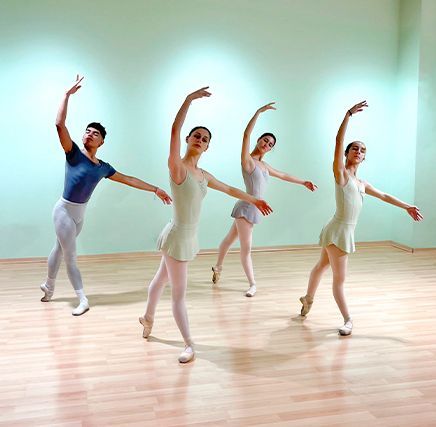 Cuatro bailarinas de ballet con leotardos en tonos pastel posan en un estudio luminoso con suelo de madera.
