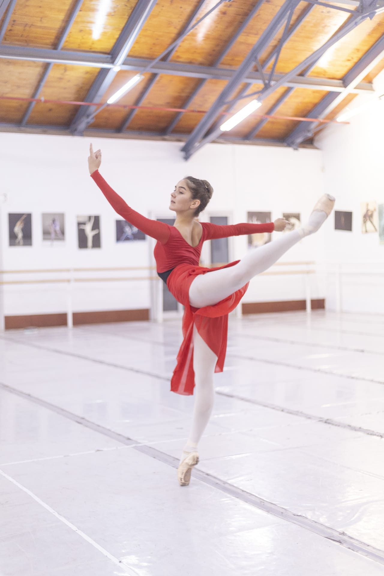 Bailarina de ballet con traje rojo posando de puntillas en un estudio luminoso.
