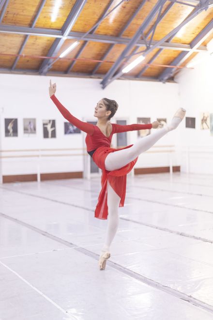Bailarina de ballet con traje rojo posando de puntillas en un estudio luminoso.