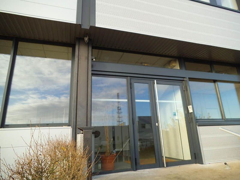 Vue extérieure d'un bâtiment avec des portes et fenêtres vitrées reflétant le ciel et un petit buisson.