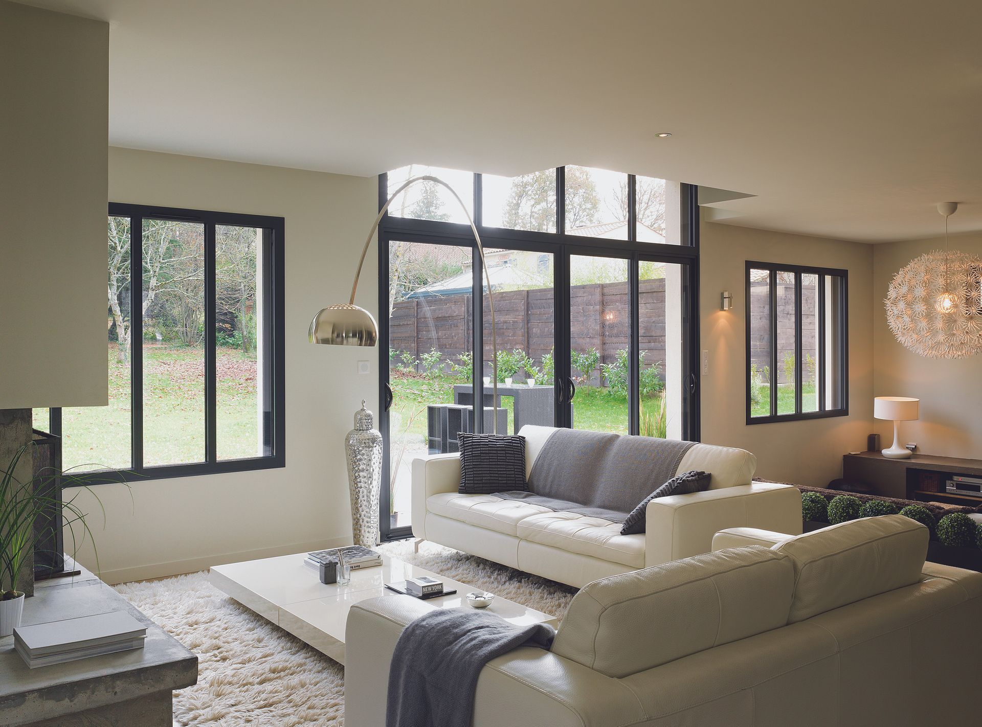 Salon avec canapés blancs, grandes fenêtres et vue sur le jardin.