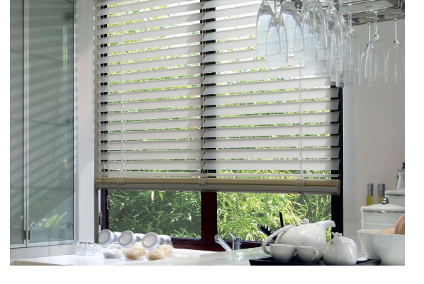 Fenêtre à stores superposés, laissant filtrer la lumière dans une cuisine avec un plan de travail et de la verrerie suspendue.