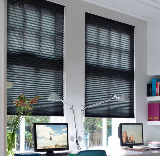 Deux stores plissés noirs dans un bureau lumineux avec des écrans d'ordinateur et des lampes de bureau.