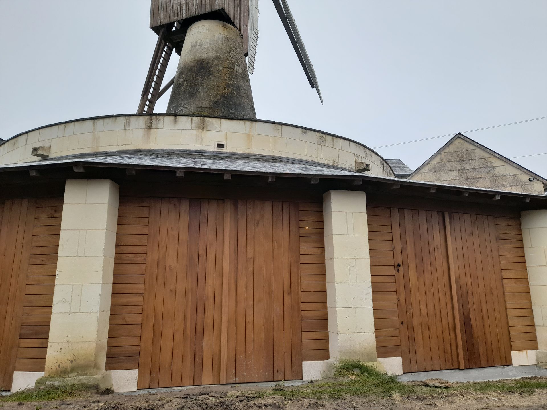 Portes en bois sous un moulin à vent aux piliers beiges. Journée nuageuse.