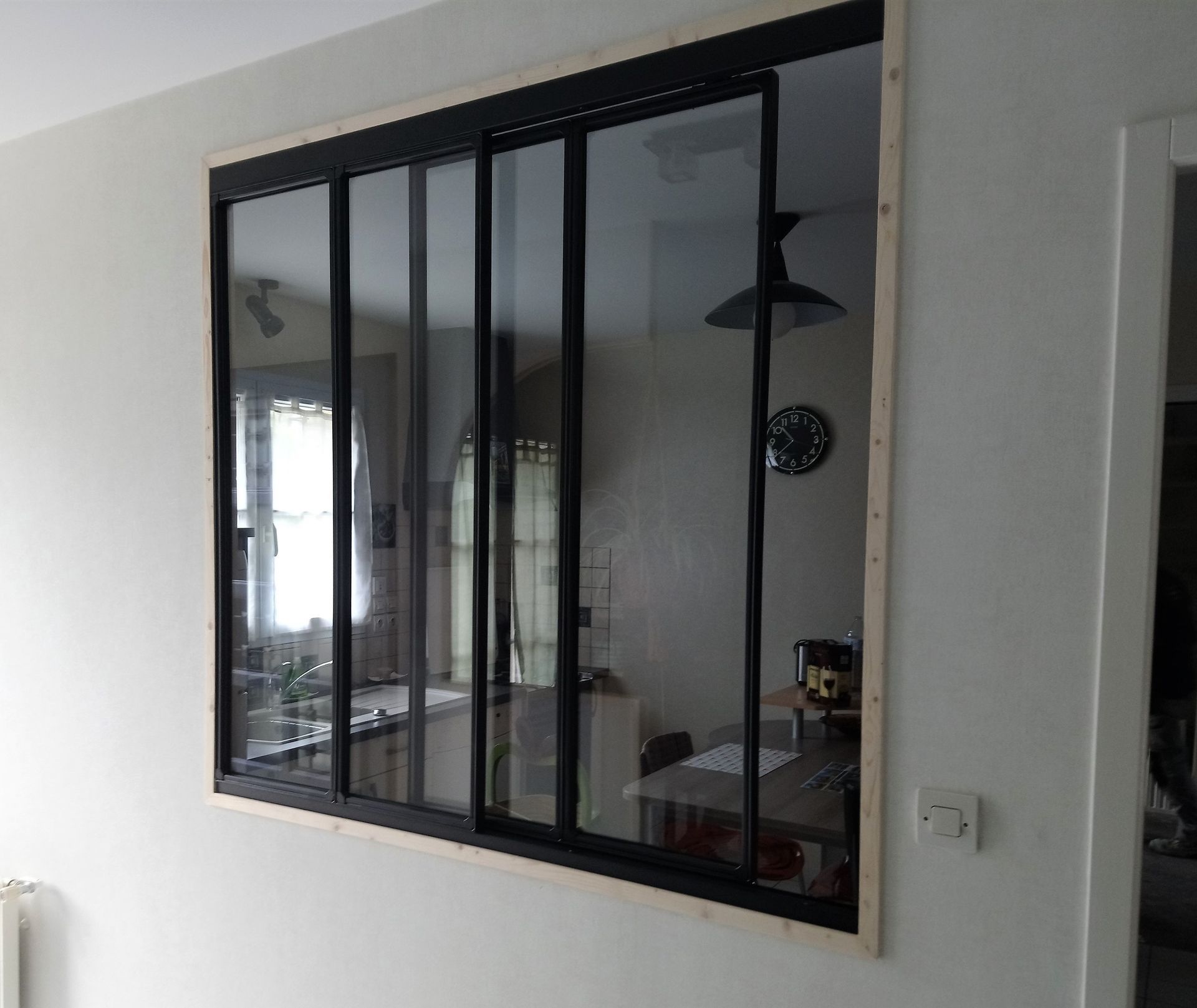 Des portes coulissantes en verre à cadre noir dans une pièce aux murs blancs, reflétant un coin repas avec une table et un luminaire.