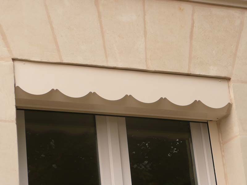 Auvent blanc festonné au-dessus d'une fenêtre blanche dans un bâtiment en pierre.