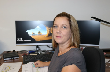 Eine Frau sitzt an einem Schreibtisch vor einem Computermonitor.