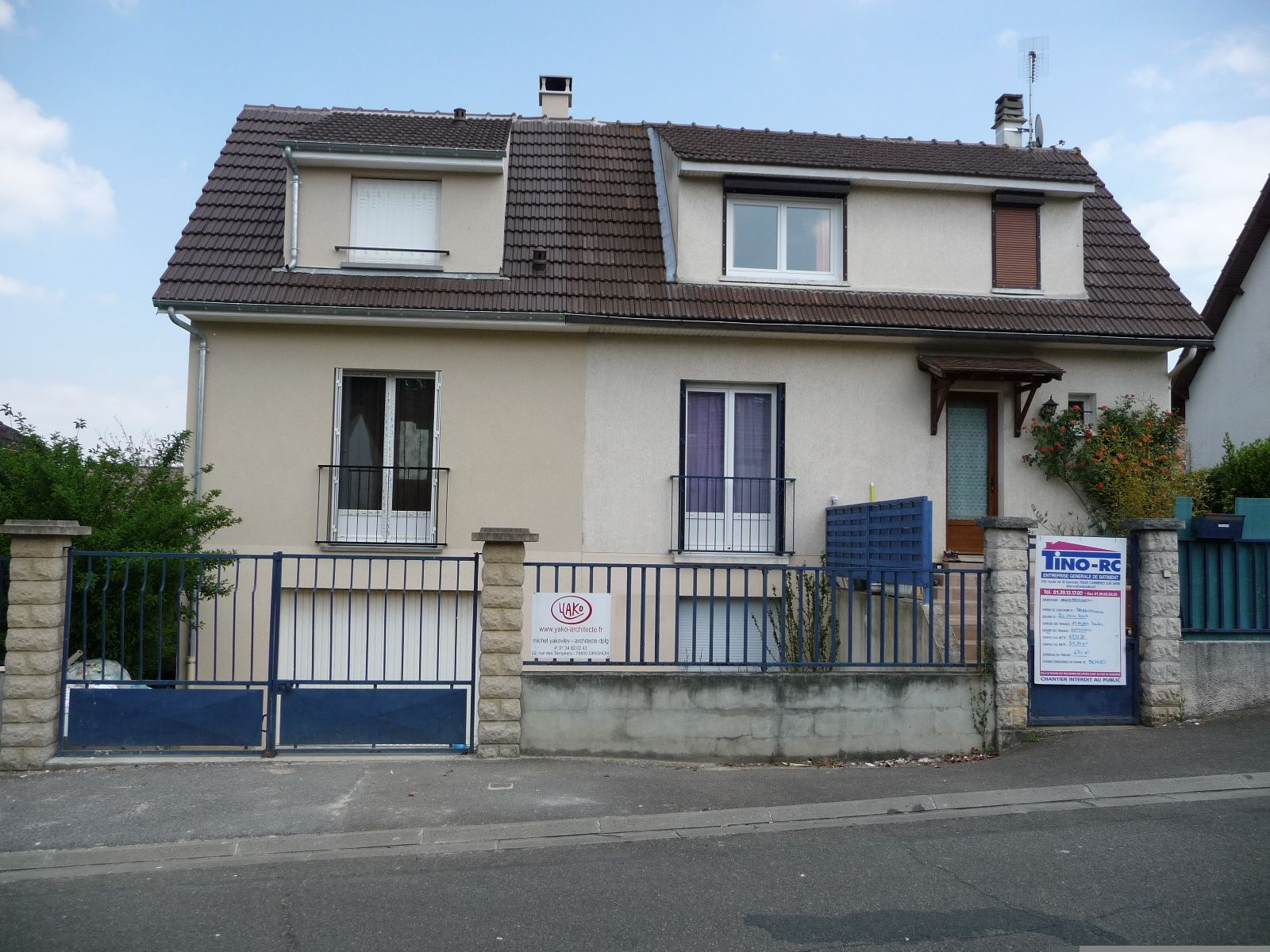 Grande maison au portail bleu avec un panneau de déclaration de travaux.