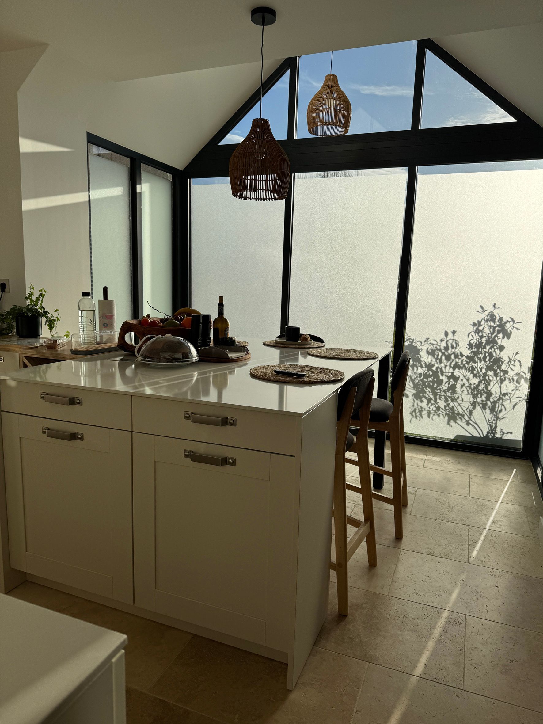 Îlot central dans une cuisine devant de grandes fenêtres au verre fumé.