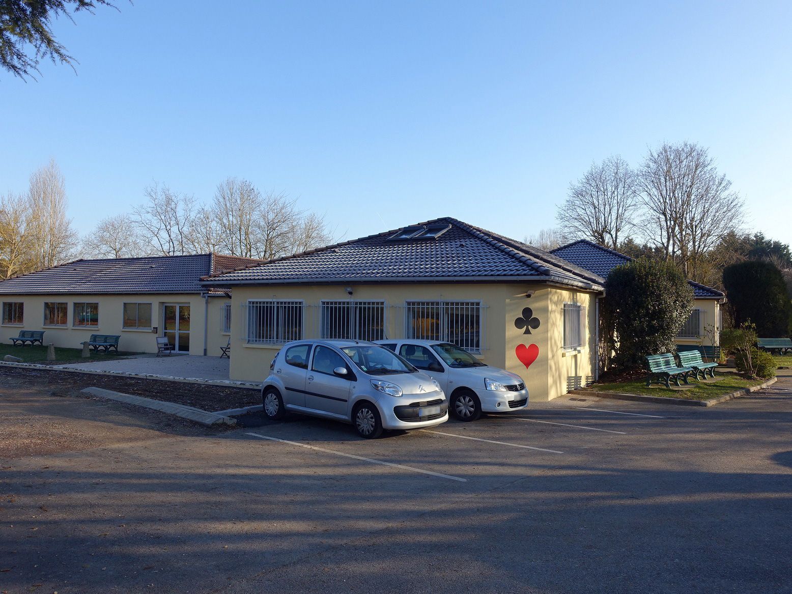 Deux véhicules gris garés devant un bâtiment aux murs beiges.