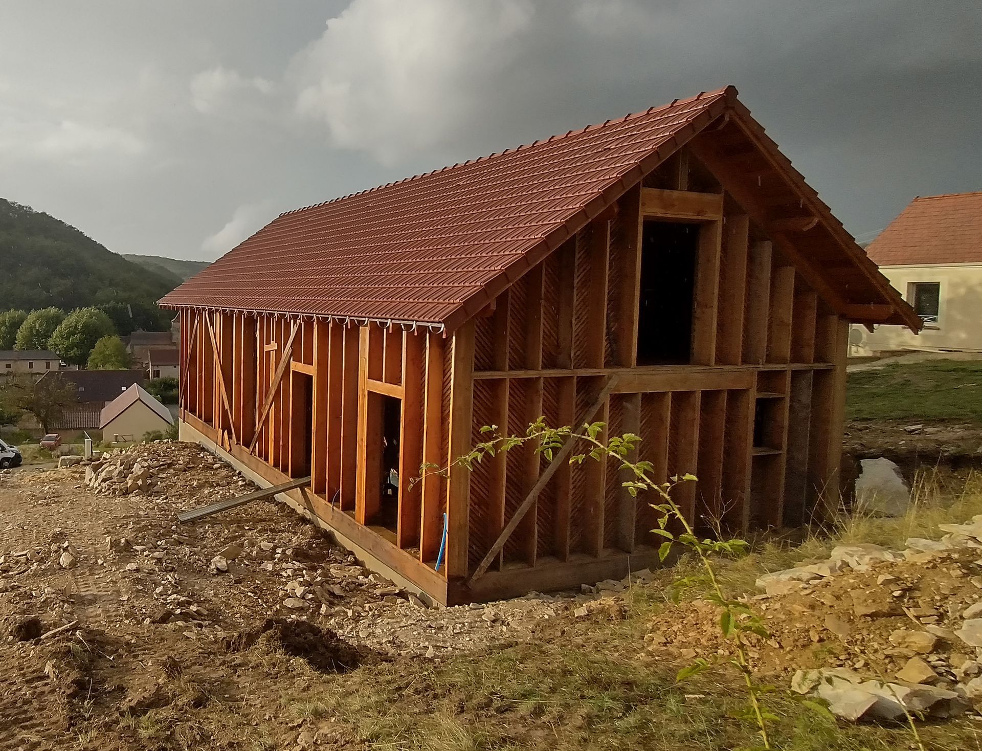 Construction en cours d'une maison en bois dont la toiture est finalisée.