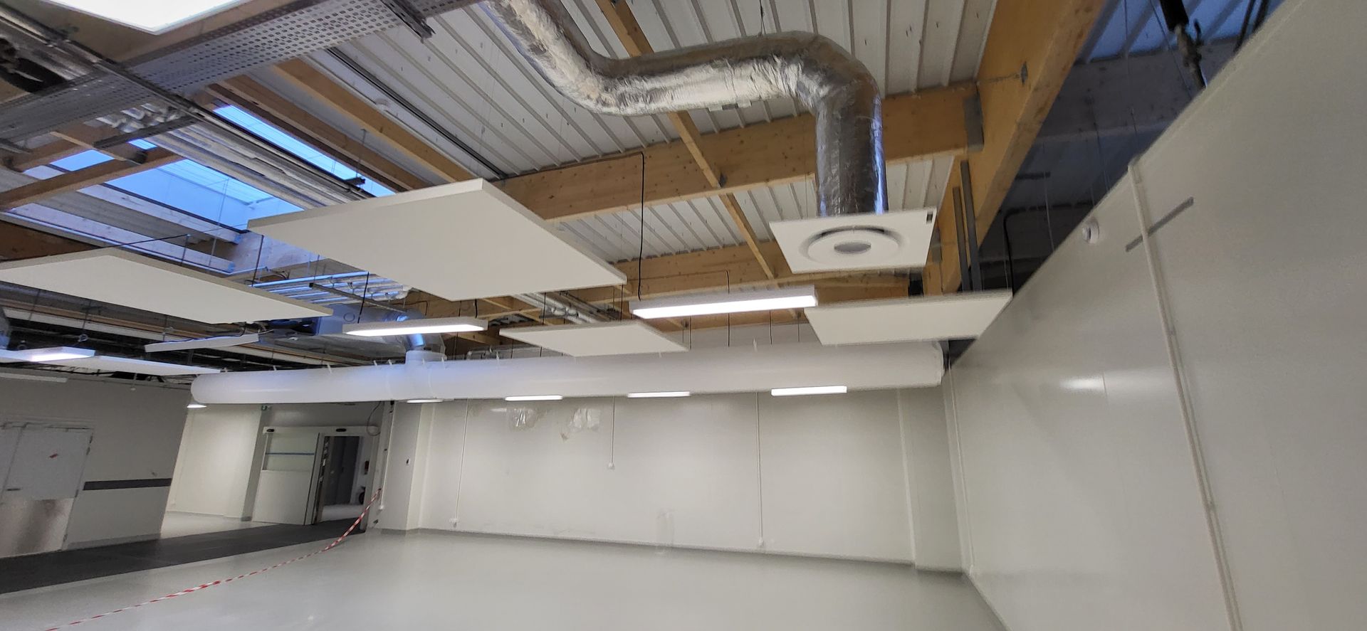 Pièce industrielle vide avec murs blancs, tuyaux apparents au plafond et panneaux acoustiques suspendus
