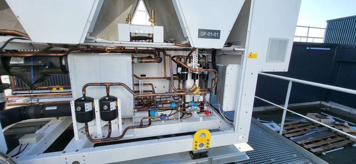 Unité de climatisation ouverte avec tuyaux, vannes et câblage apparents à l'intérieur d'un boîtier sur le toit.