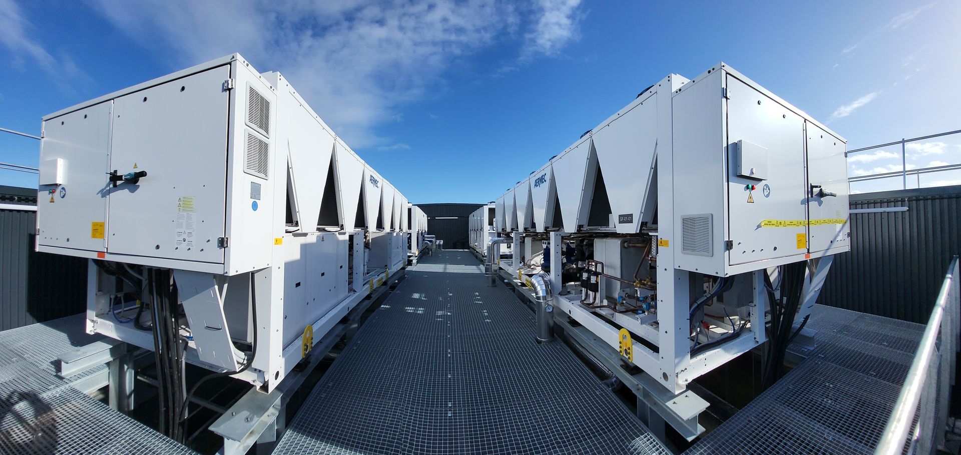 Des rangées d'unités de climatisation industrielles blanches sur un terrain gravillonné sous un ciel bleu