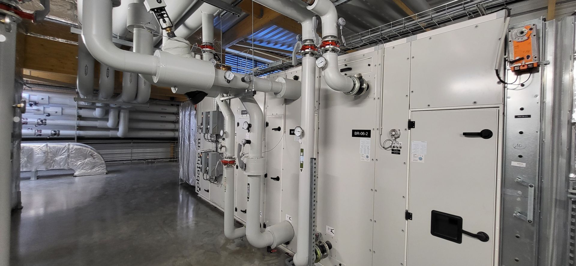 Salle des machines industrielles avec tuyaux blancs, vannes et gros équipements dans un intérieur métallique propre
