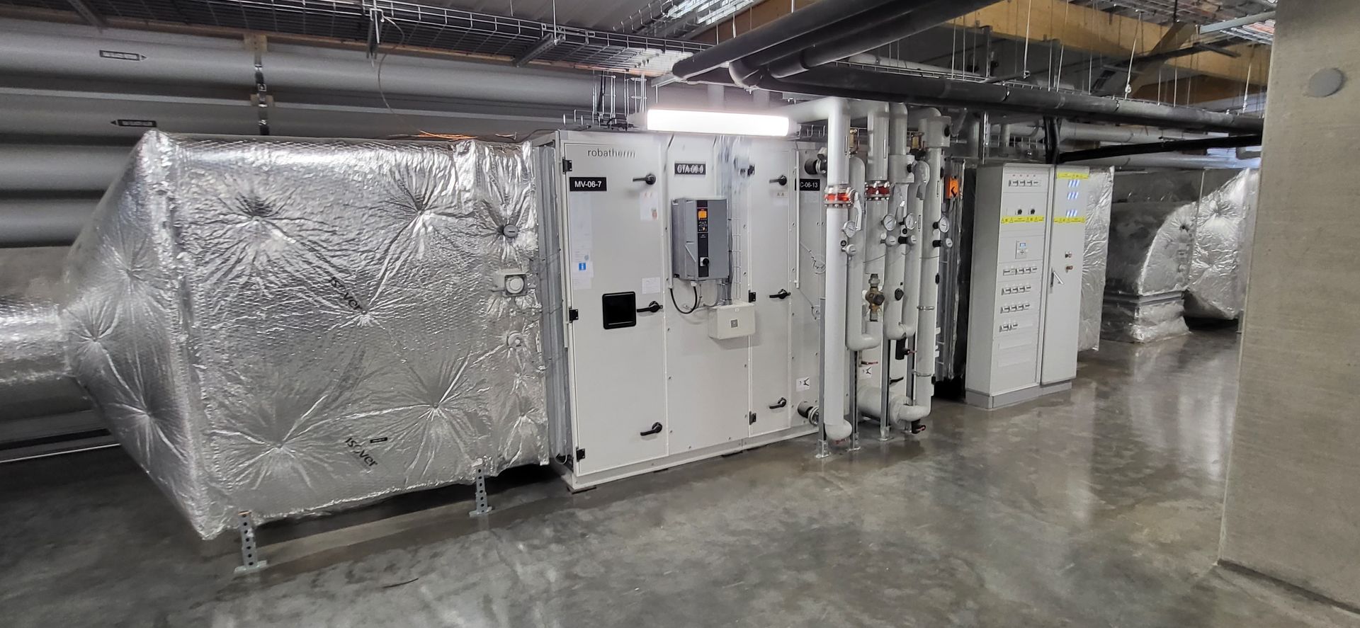 Local industriel avec unités de climatisation isolées, tuyauterie et équipements le long d'un sol en béton