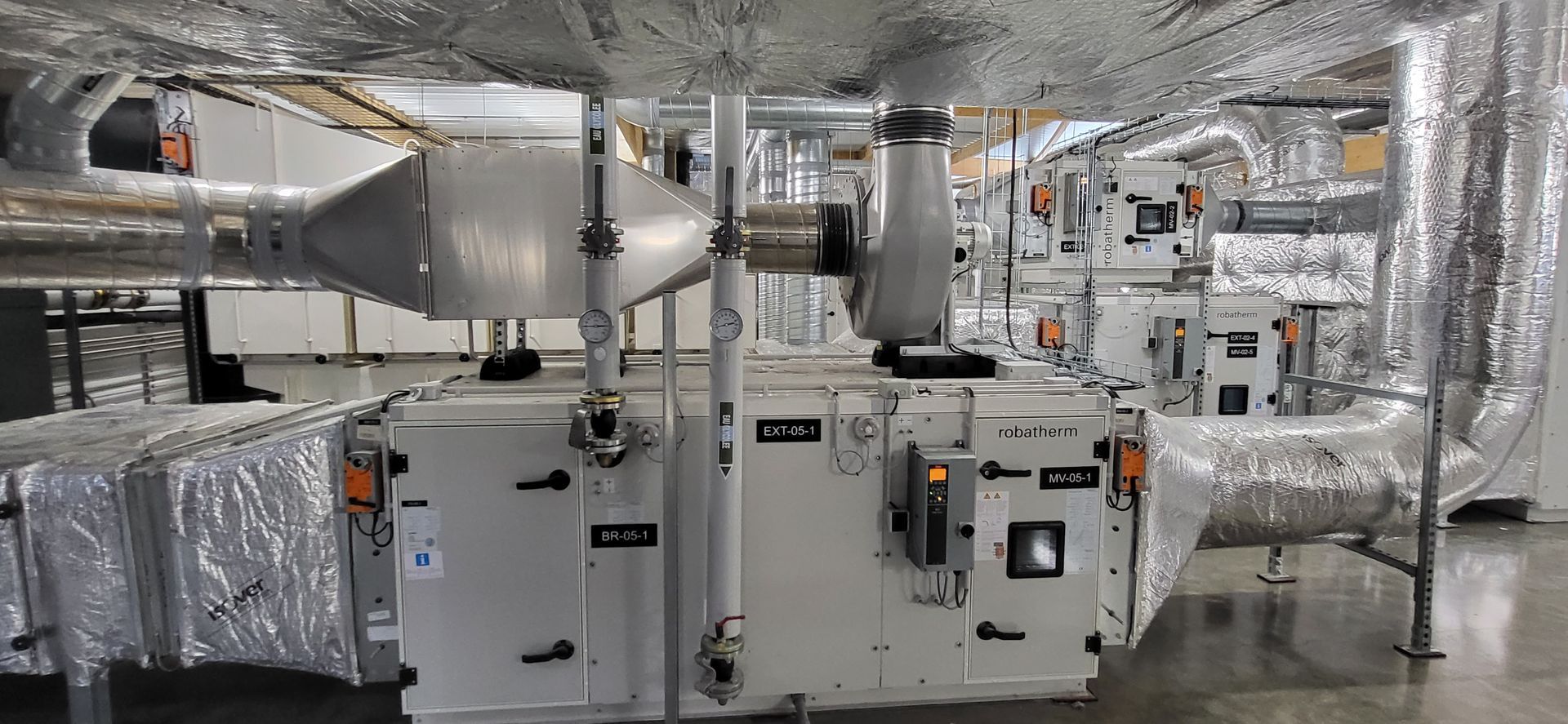 Unités de climatisation industrielles et grands conduits argentés dans une salle des machines avec isolation en aluminium et tuyauterie
