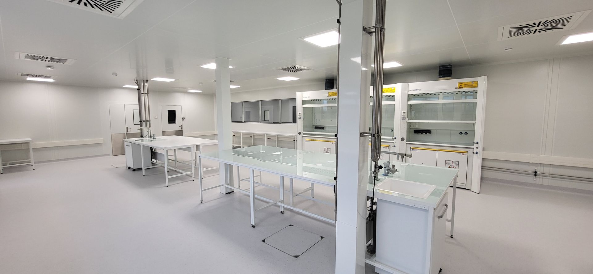 Laboratoire lumineux et propre avec des paillasses blanches, des cloisons en verre et des équipements dans un espace de travail moderne