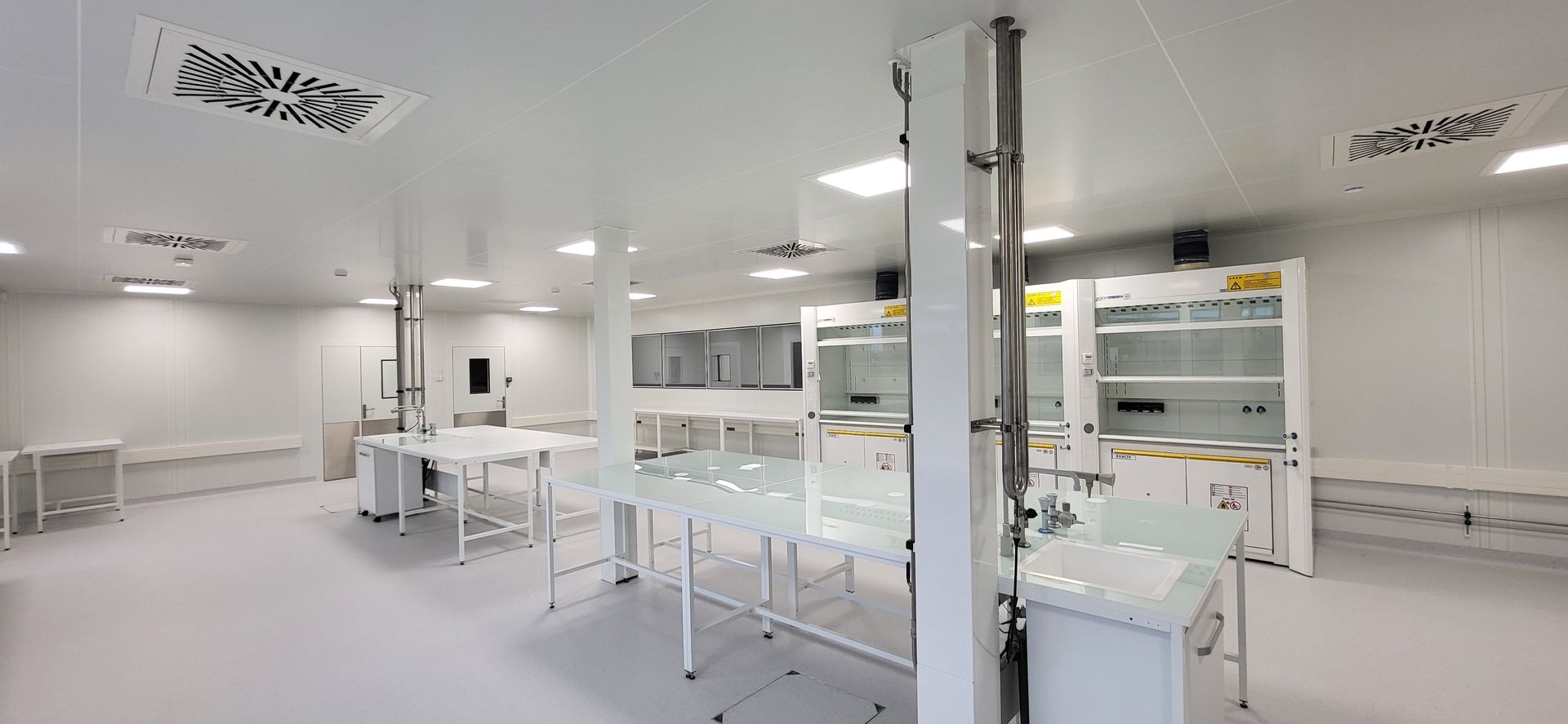 Laboratoire moderne et lumineux, d'un blanc éclatant, avec paillasses, armoires et équipements éclairés par des néons.