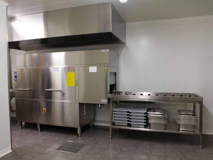 Cuisine professionnelle équipée d'appareils en acier inoxydable, d'une hotte aspirante et d'une table de préparation en métal avec plateaux.