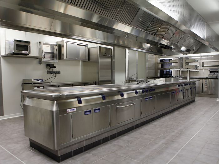 Cuisine commerciale en acier inoxydable avec comptoirs, fours et hottes aspirantes dans une zone de préparation de restaurant propre