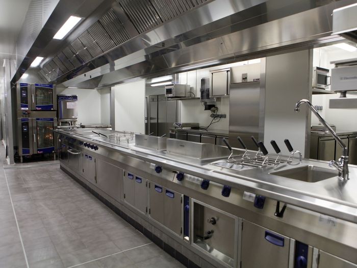 Cuisine commerciale moderne avec comptoirs en acier inoxydable, éviers et système de ventilation par le haut.