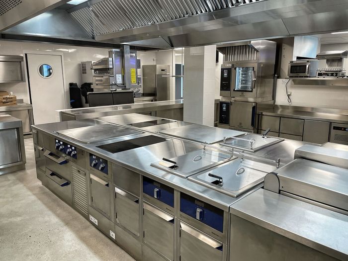 Cuisine commerciale moderne en acier inoxydable avec cuisinière, fours et comptoirs.