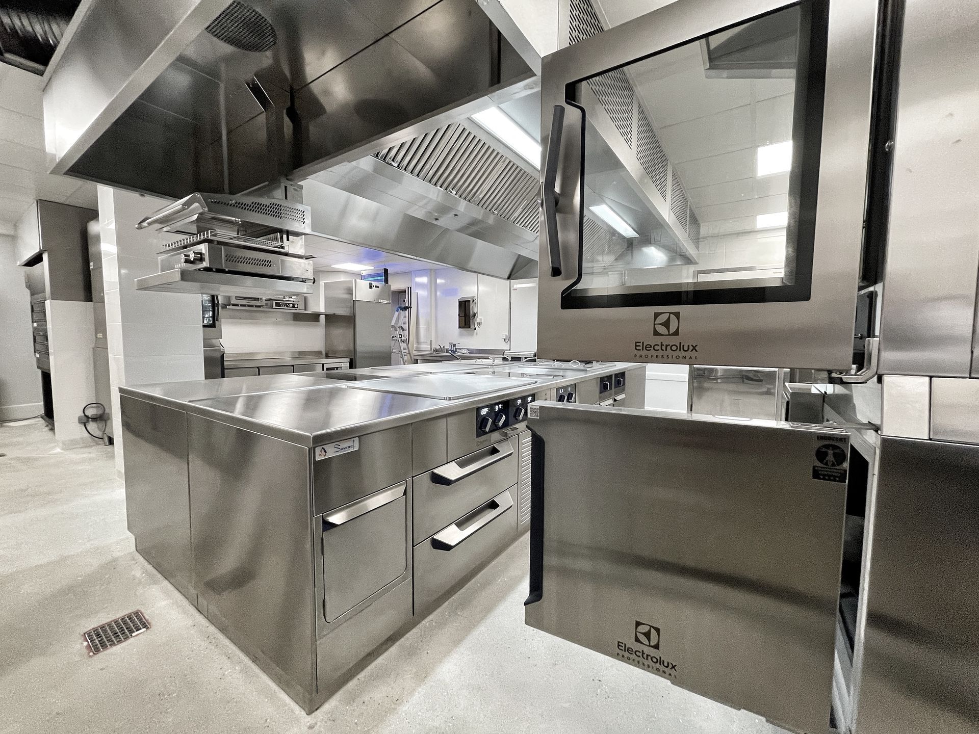 Cuisine commerciale en acier inoxydable avec appareils de cuisson, hotte aspirante et passe-plat.