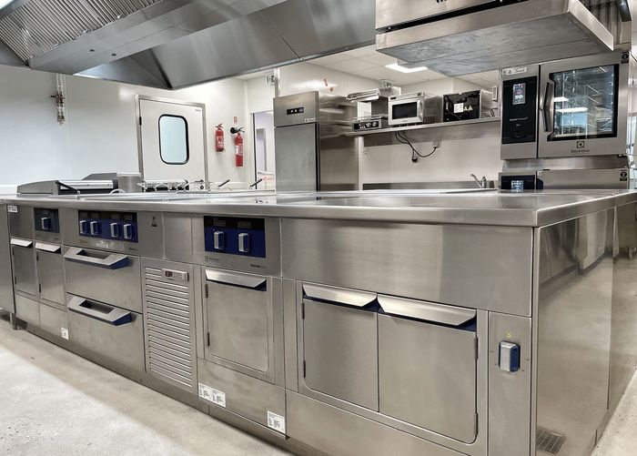 Cuisine commerciale en acier inoxydable avec comptoirs, fours et hotte aspirante dans un espace industriel propre
