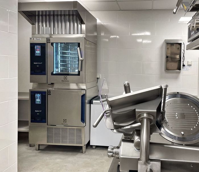 Cuisine professionnelle avec fours en acier inoxydable et trancheuse industrielle sur un sol carrelé.