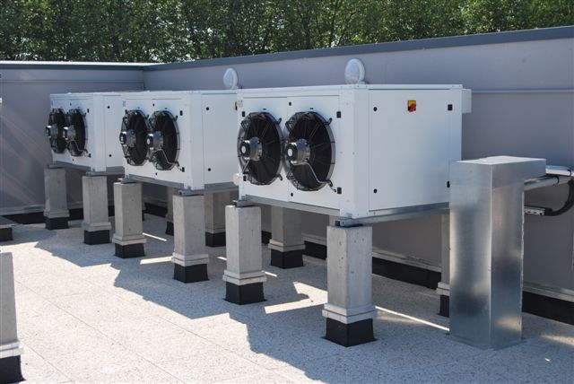 Unité de climatisation sur le toit, équipée de plusieurs grands ventilateurs montés sur des supports métalliques, installée à l'extérieur contre un mur.