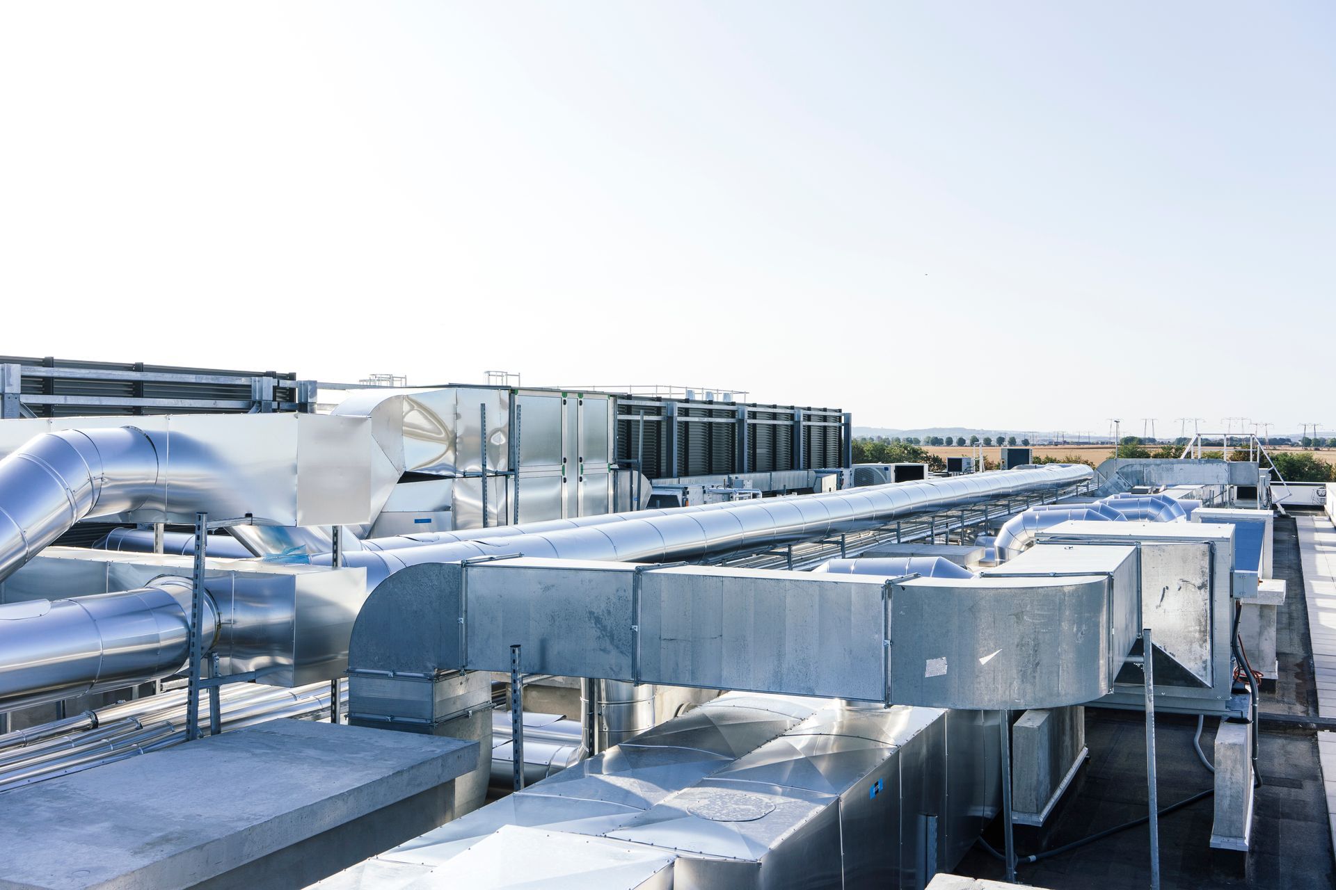 Toit industriel avec de grands conduits de ventilation argentés et des équipements de ventilation sous un ciel lumineux