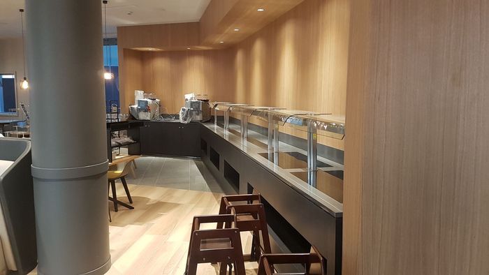 Intérieur de café moderne avec murs en bois, vitrine à pâtisseries et quelques tabourets le long du comptoir.