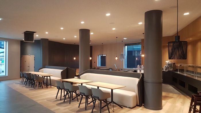 Salon moderne avec de longues tables, des banquettes blanches, des colonnes sombres et un éclairage chaleureux au plafond.