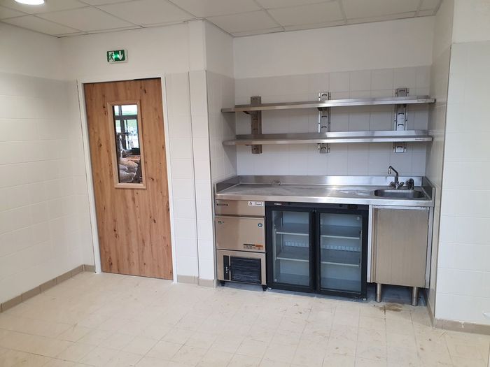 Petite kitchenette avec évier, étagères, placards et porte en bois dans une pièce simple.