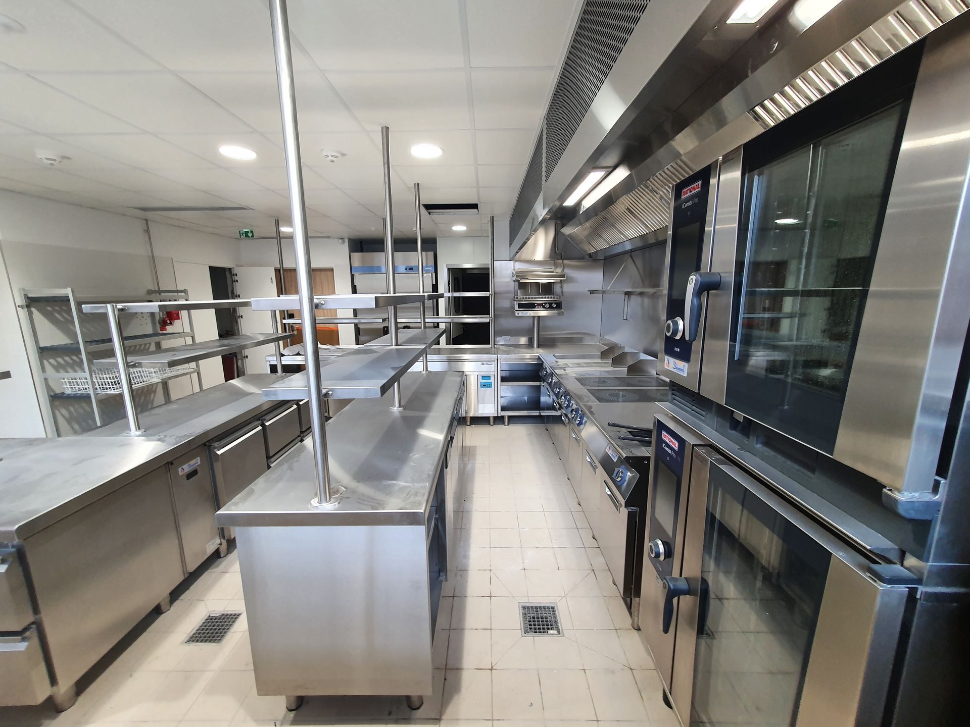 Cuisine commerciale vide avec comptoirs en acier inoxydable, fours et tables de préparation sous un éclairage zénithal intense