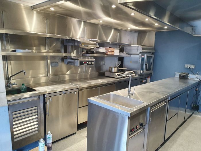 Cuisine commerciale en acier inoxydable avec comptoirs, éviers, fours et un mur bleu.