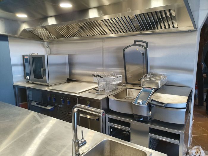 Cuisine professionnelle avec comptoirs en acier inoxydable, fours et grande hotte aspirante.