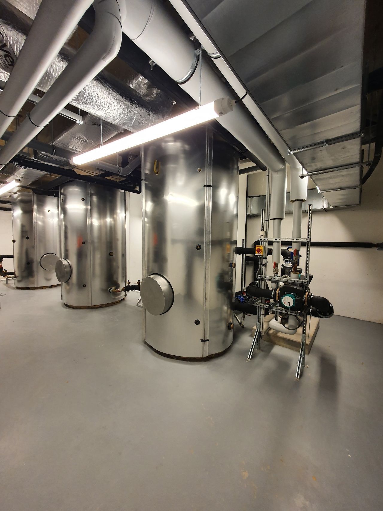 Salle industrielle avec de grandes cuves en acier inoxydable, des tuyaux et des machines sur un sol gris