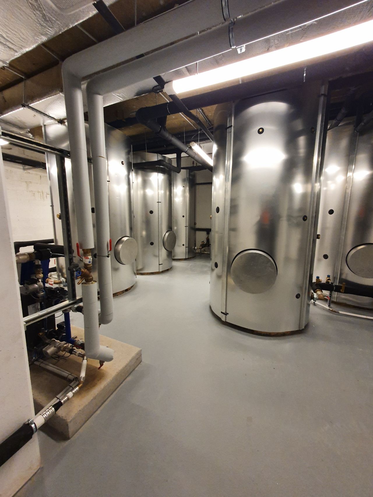 Sous-sol industriel avec de grandes cuves en acier inoxydable, des tuyaux et un sol gris