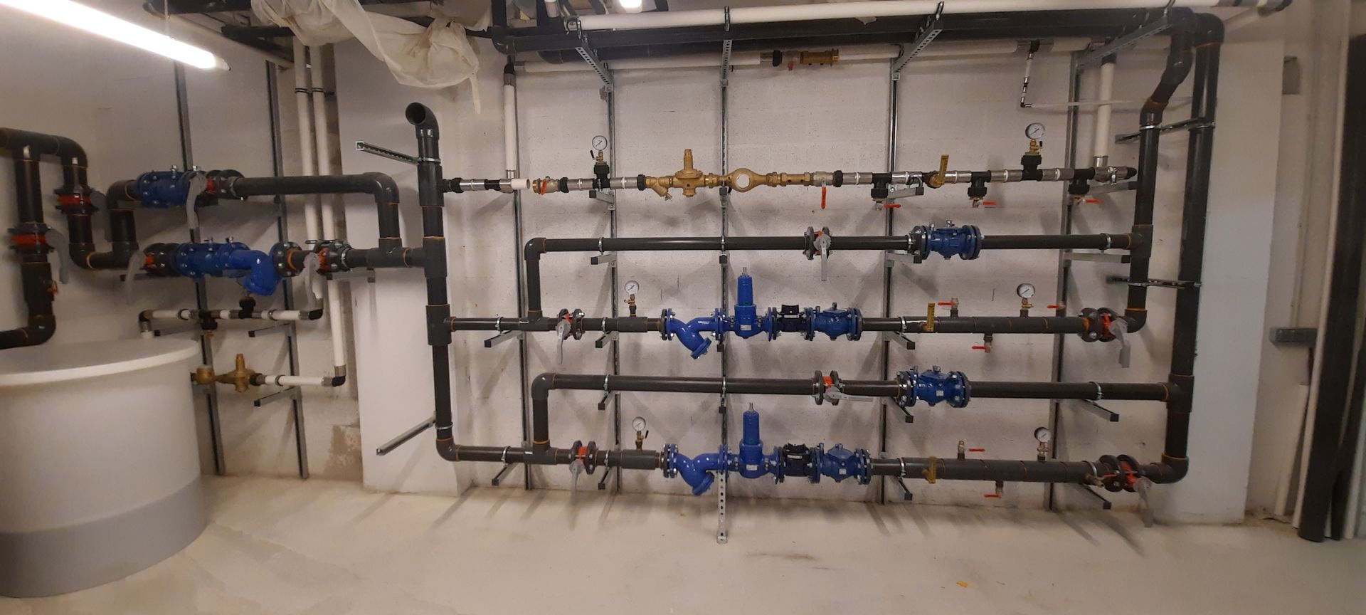 Système industriel de filtration d'eau et de tuyauterie avec réservoirs gris et vannes bleues le long d'un mur